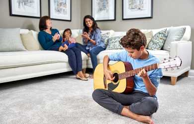 boy plays guitar on clean carpets while family sits on couch