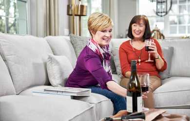 two women enjoy wine while sitting on a couch